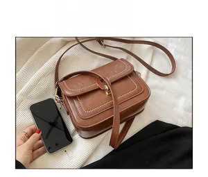 Détail du sac à bandoulière en cuir marron avec surpiqûres blanches et boucle en métal