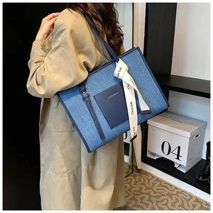 Detail of denim tote bag featuring leather pocket and decorative white silk scarf