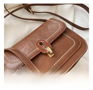 Détail du sac en cuir litchi marron avec surpiqûres et fermoir ovale doré brillant