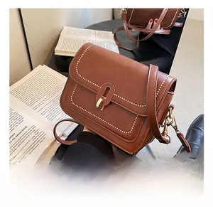 Détail du sac en similicuir caramel avec clous dorés et boucle sur des livres vintage