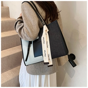 Detail of large denim tote bag featuring color-block design and stylish ribbon on shoulder