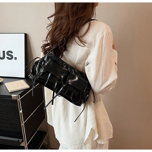 Detail of black glossy baguette bag featuring elegant bow-tie ribbons and pleated texture