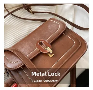 Gros plan du fermoir doré et des surpiqûres blanches sur le sac bandoulière marron en cuir
