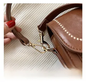 Vue macro du crochet doré poli et des surpiqûres sur le sac bandoulière en cuir brun
