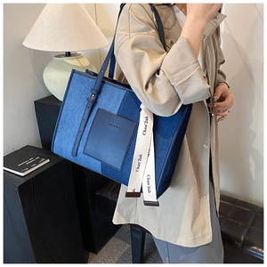 Detail of blue denim tote bag with leather pocket and side strap branding on a desk