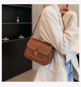 Détail du sac bandoulière en cuir marron avec surpiqûres et fermoir ovale doré