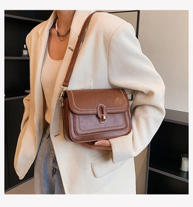 Détail d'un sac à bandoulière marron foncé avec fermoir en métal doré et surpiqûres