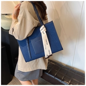 Detail of a large dark blue denim tote bag with leather pocket and branded webbing strap