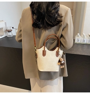 Borsa a secchiello beige con manici marroni e ciondolo di peluche su un blazer