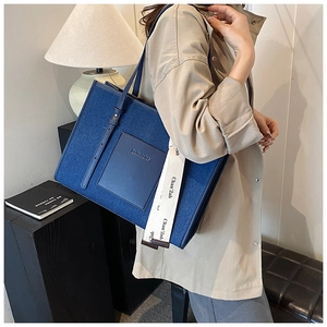 Detail of blue denim tote bag with leather pocket and adjustable shoulder strap