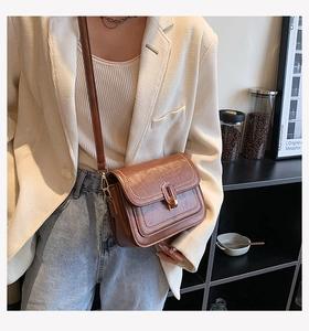 Détail d'un sac bandoulière en cuir marron avec surpiqûres blanches et boucle dorée