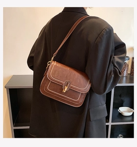 Détail d'un sac bandoulière marron avec surpiqûres blanches et fermoir doré