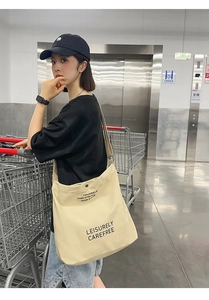 Detailed shot of a cream canvas tote bag with black text used as a shoulder bag