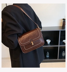 Gros plan du sac en cuir marron avec surpiqûres blanches et fermoir doré tournant