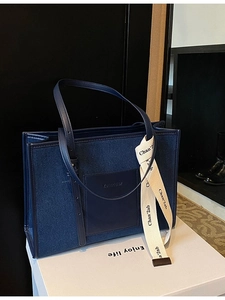 Navy denim tote bag with leather pocket and decorative ribbon on display stand