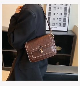 Gros plan d'un sac bandoulière vintage marron avec surpiqûres blanches et boucle dorée