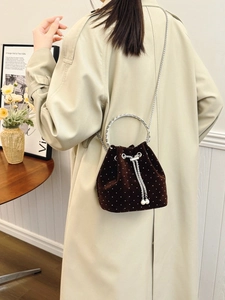 Brown velvet bucket bag with pearls and chain strap worn with a beige trench coat