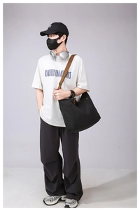 Detail of black canvas messenger bag with adjustable brown strap and metal buckle