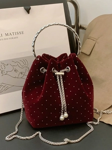 Burgundy velvet bucket bag with silver studs and pearl drawstring on artistic background