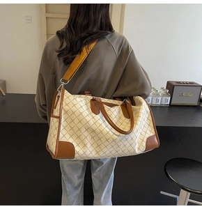 Detail der karierten Reisetasche mit orangefarbenem Gurt und Lederverstärkung