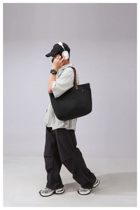 Detailed view of black canvas tote bag with brown leather handles and front pocket