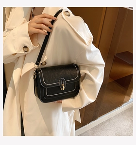 Détail du sac bandoulière noir avec coutures contrastées blanches et fermoir doré