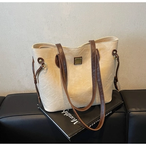 Makroansicht der beigen Shopper-Tasche mit braunem Lederbesatz und goldener Metallplatte