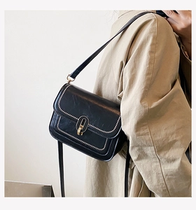 Détail d'un petit sac carré en cuir ciré noir avec clous dorés et fermoir ovale