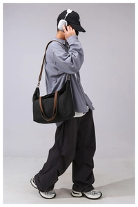 Detail of black canvas crossbody bag with brown leather handles and adjustable strap