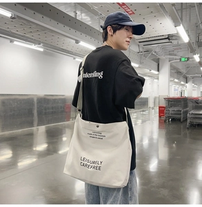 Detailed close-up of large beige canvas messenger bag featuring black printed lettering