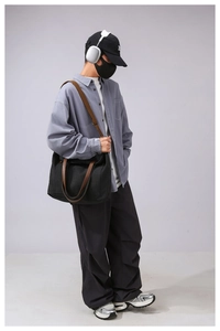 Detail of large black canvas tote bag with brown leather handles worn by model