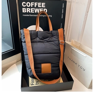 Detail of black quilted puffer bucket bag with brown leather straps and square patch