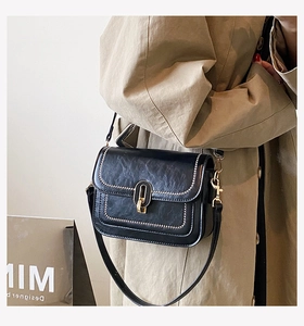 Détail du sac bandoulière noir avec fermoir doré et rivets sur trench-coat kaki