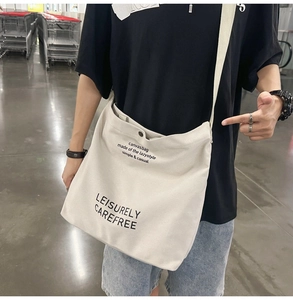Detail of off-white canvas crossbody bag featuring black graphic text print and strap