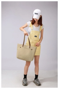 Detail of khaki canvas tote bag featuring brown leather handles and a riveted outer pocket