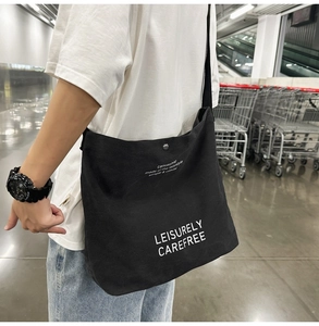 Close-up of black canvas crossbody bag with white text and metal magnetic snap button