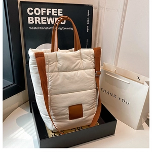 Detail of white quilted puffer bucket bag with brown leather handles and wide shoulder strap
