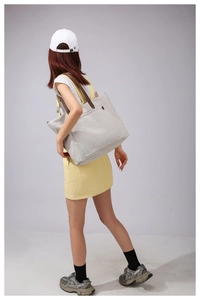 Detail of a large off-white canvas tote bag featuring brown handles and front zipper pocket