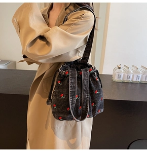 Detail of a denim bucket bag featuring red cherry embroidery and drawstring closure