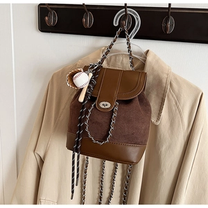Detail of a brown matte leather mini backpack with chain strap and baseball charm