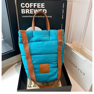 Detail of blue quilted puffer bucket bag with brown leather straps and square logo tag