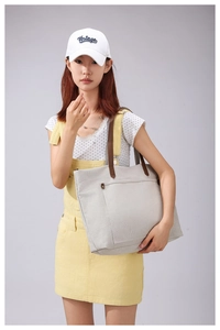 Asian model styling a large cream canvas tote bag with brown leather straps in a studio