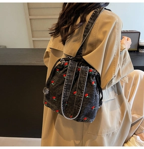 Detail of dark grey denim bucket bag with red cherry embroidery and drawstring closure