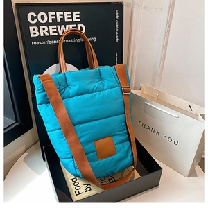 Macro shot of blue quilted puffy bucket bag with brown leather accents and straps