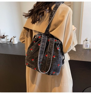Detail of denim bucket bag with red cherry embroidery and drawstring on a model