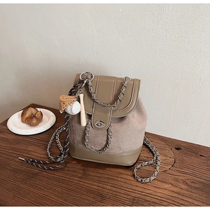 Detail of khaki bucket backpack with chain strap and baseball charms on wooden table