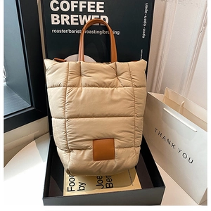Detail of light beige quilted bucket bag with synthetic leather handles in lifestyle setting