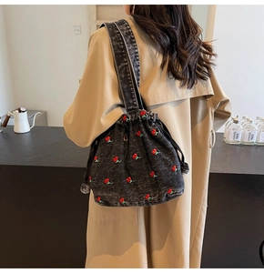 Detail view of denim bucket bag featuring red cherry embroidery and drawstring closure