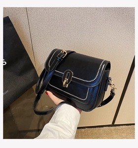 Détail d'un sac bandoulière noir avec fermoir métallique et bordure cloutée