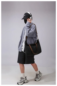 Detail of black canvas tote bag with brown leather straps shown on a female model